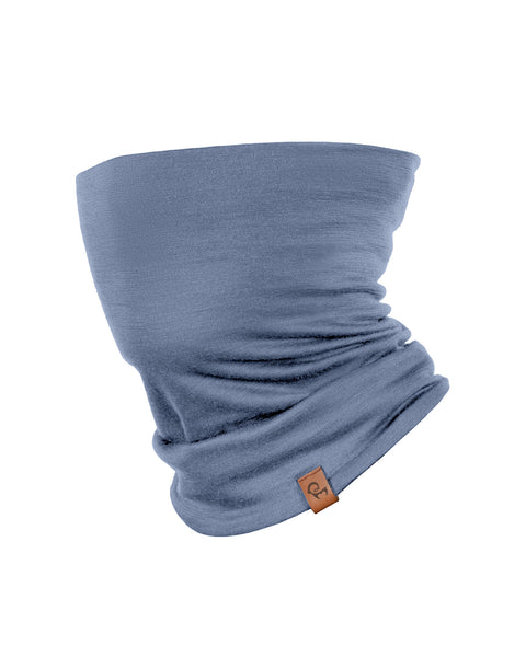 A product shot of a dusty blue tubular neck gaiter displayed upright against a pure white background. The fabric shows natural folds and draping, with a small brown leather logo patch attached near the bottom right edge.