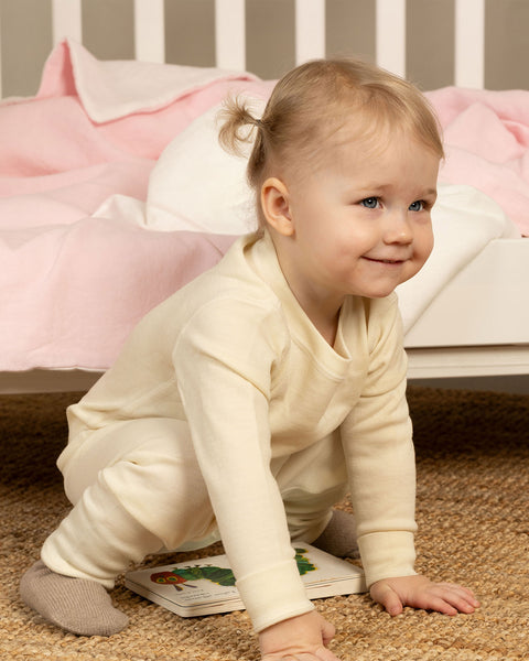 little girl in natural color matching merino thermal set smiling sitting on the floor
