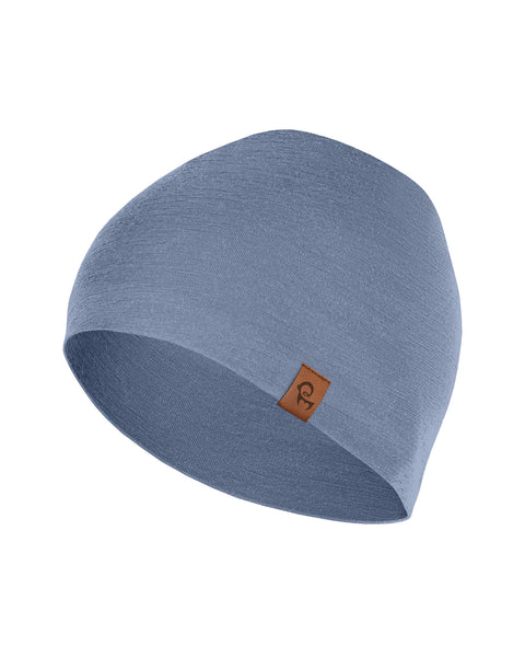 A product shot of a solid dusty blue beanie hat against a pure white background. The fabric is smooth, and the hat features a small, square brown leather logo patch on the lower right edge.