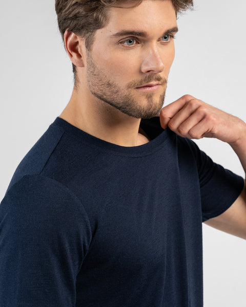 A close-up side profile of a man looking off to the right. He is pulling lightly at the neckline of his dark navy blue short-sleeved t-shirt.