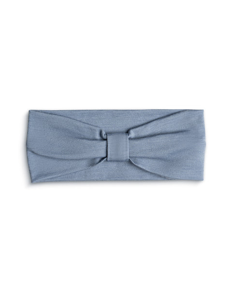 A product shot of a dusty blue fabric headband laid flat against a plain white background. The headband features a gathered center detail with a matching fabric wrap, creating a subtle bow or ribbon effect.