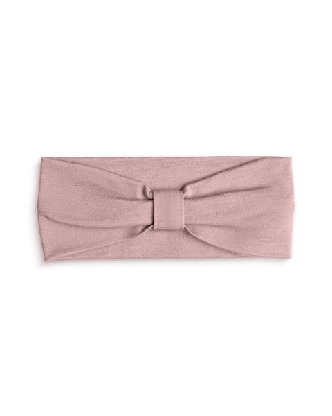 A product shot of a dusty pink fabric headband laid flat against a plain white background. The headband features a gathered center detail with a matching fabric wrap, creating a subtle bow or ribbon effect.