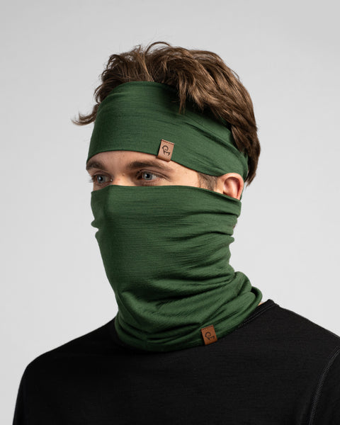 A studio portrait of a man looking off to the left. He is wearing a black long-sleeved shirt, a dark green headband, and a matching dark green neck gaiter pulled up to cover his mouth and nose.
