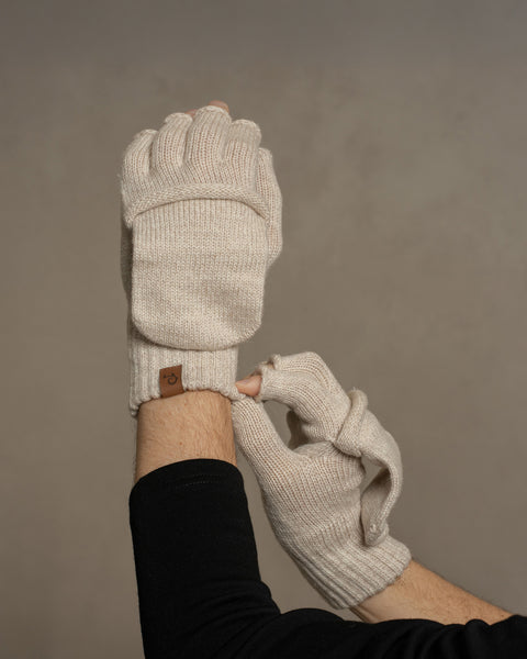Creamy beige merino wool convertible gloves worn on hands, showing fingerless design with fold-over mitten flap for adjustable warmth.