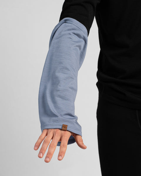 A close-up shot showing a person's right arm extended downward. They are wearing a black long-sleeved shirt with a dusty blue neck gaiter pulled over their forearm, extending down past their wrist.