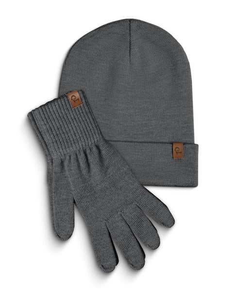 A dark gray knitted beanie and a pair of matching gloves are laid flat against a white background. Both the beanie and each glove have a small, rectangular brown leather tag with a menique logo on them. The items are slightly overlapping, with the beanie positioned above and to the left of the gloves.