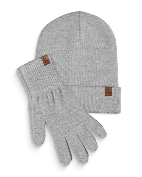 A light gray knitted beanie and a pair of matching gloves are laid flat against a white background. Both the beanie and each glove have a small, rectangular brown leather tag with a menique logo on them. The items are slightly overlapping, with the beanie positioned above and to the left of the gloves.