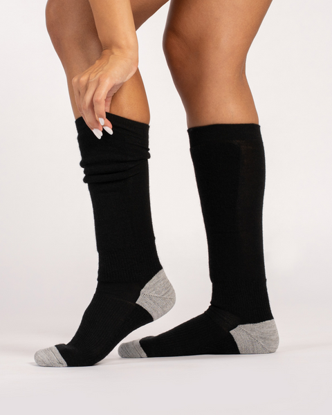 Women wearing black knee-high skii merino wool socks with gray toes on a white background