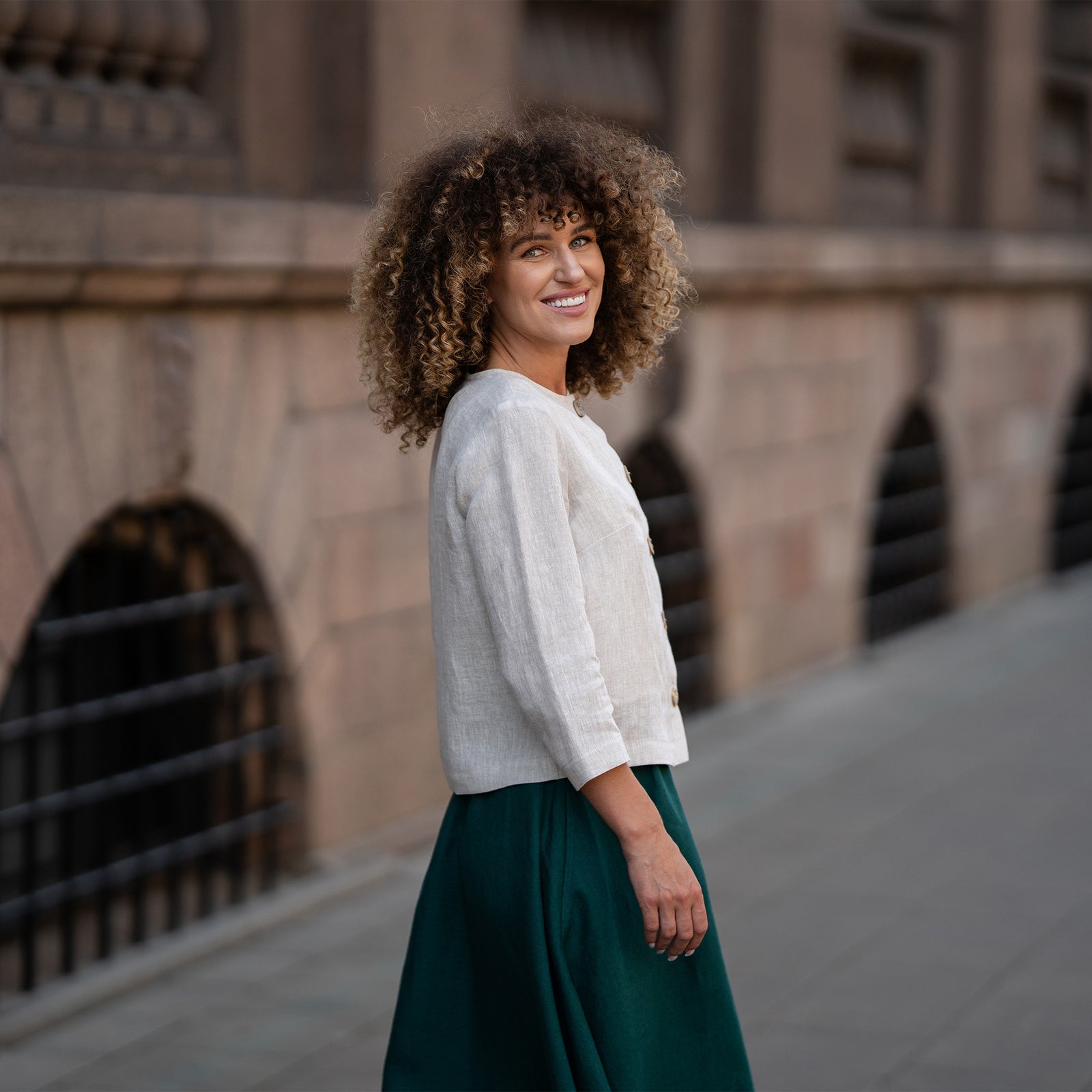 A model wearing a natural beige linen jacket Alice with buttons, featuring a relaxed fit, 3/4-length sleeves, and a minimalist design. The jacket is paired with matching dark green skirt