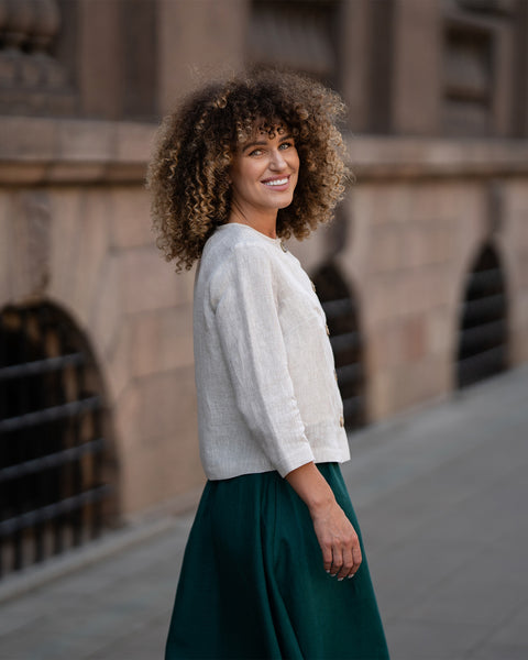 A model wearing a natural beige linen jacket Alice with buttons, featuring a relaxed fit, 3/4-length sleeves, and a minimalist design