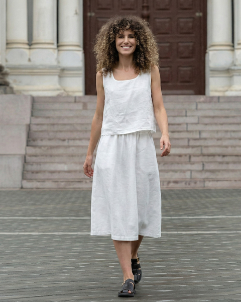 Woman wearing white linen two-piece set with sleeveless top and flowy midi skirt, sustainable breathable summer outfit styled in urban setting