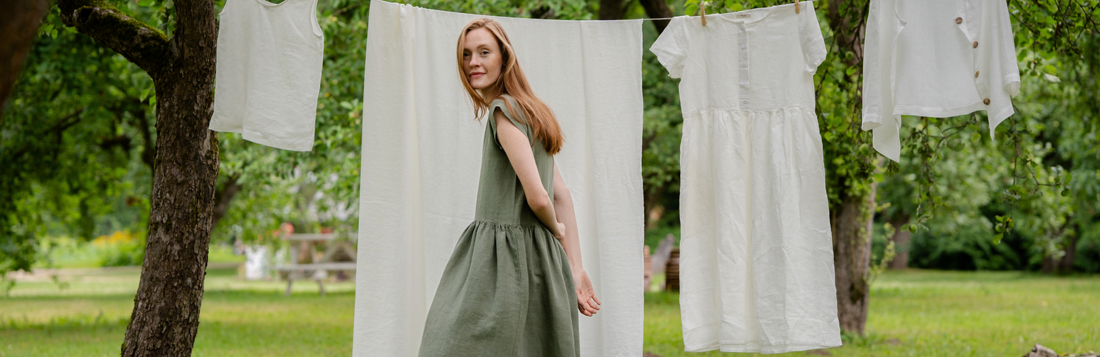 Woman in green linen dress near outdoor clothesline with natural fabrics