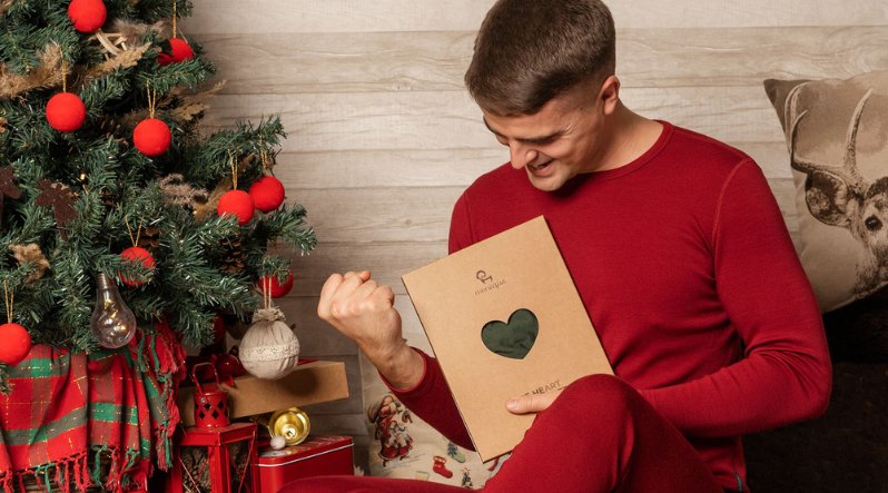 Man in red loungewear holding gift, sitting in cozy holiday setting
