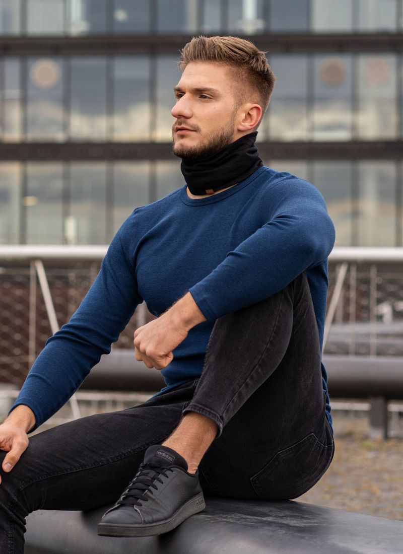 Man wearing a blue sweater and black pants sitting on a ledge with a cityscape background