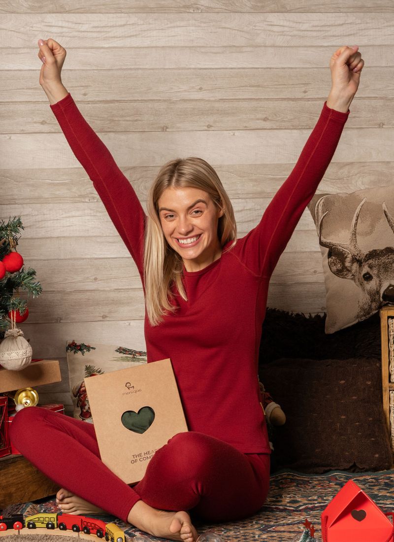 Happy woman in red loungewear celebrating with gift box indoors