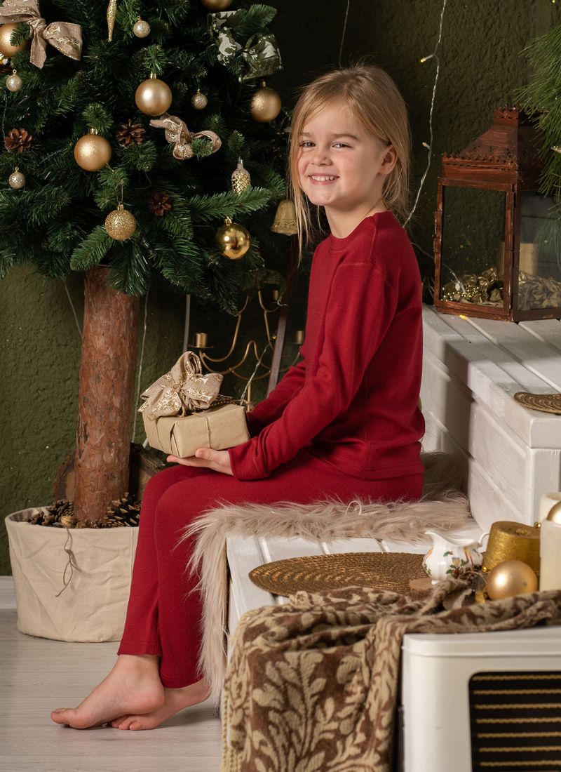 Smiling girl in red loungewear holding gift near decorated Christmas tree