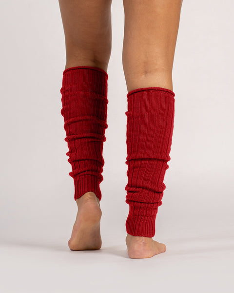 Close-up of red ribbed wool leg warmers worn barefoot, showing soft knit texture and slouchy fit.