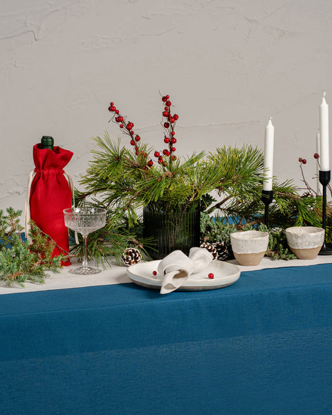 The menique linen tablecloth in cobalt blue color. The tablecloth drapes over a wooden table