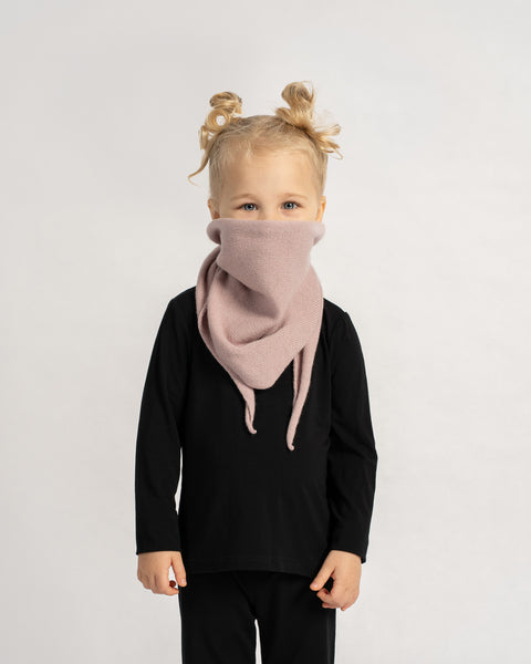 Child wearing a pink knit headscarf, smiling and posing in a black outfit against a plain background.