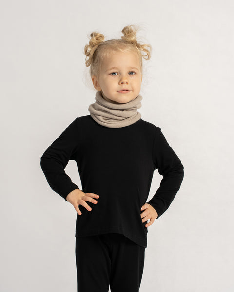 Child wearing a beige knit neck warmer with a black outfit, posing confidently with hands on hips.