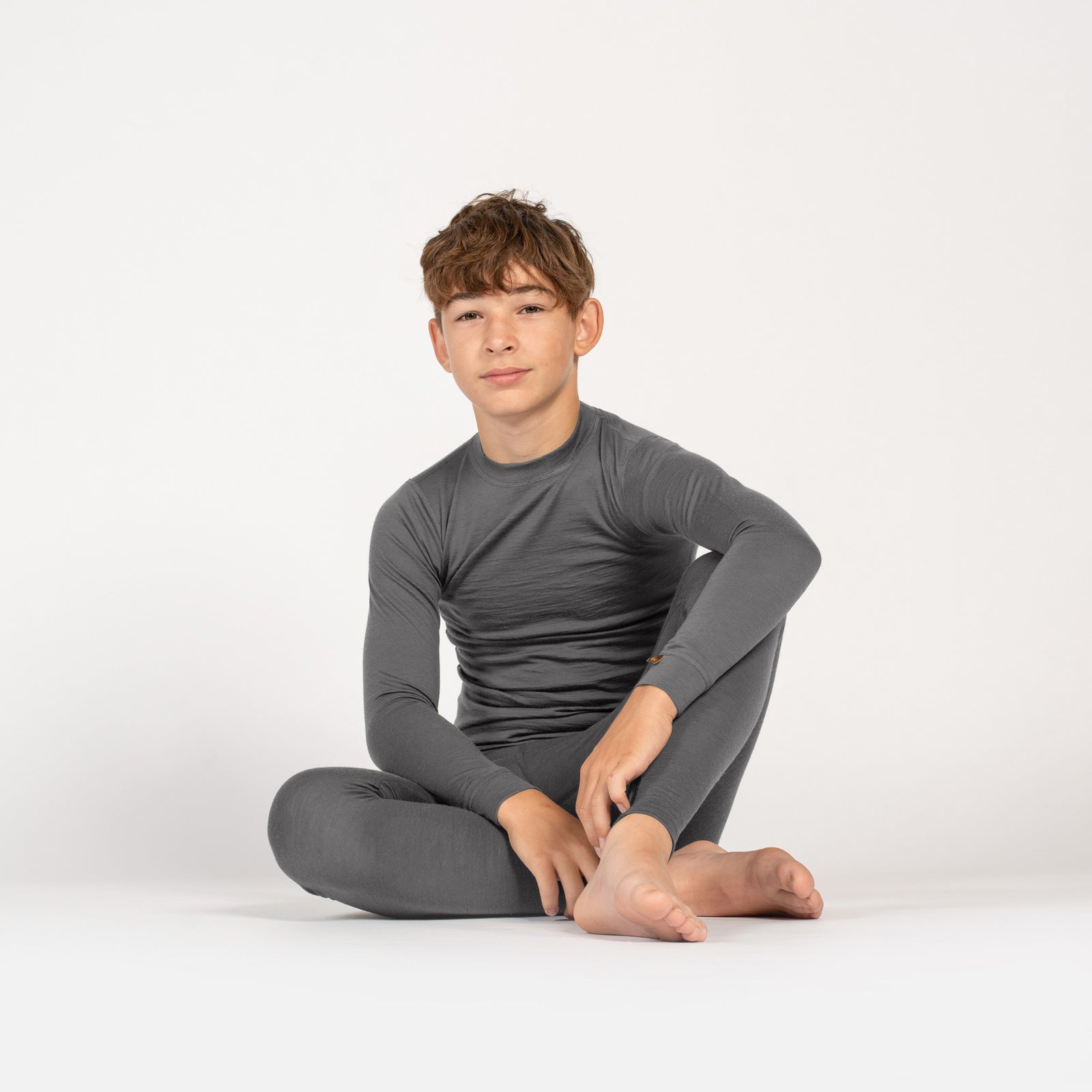 Smiling girl in gray Merino wool base layer set standing on a yellow armchair, playing with her braids.