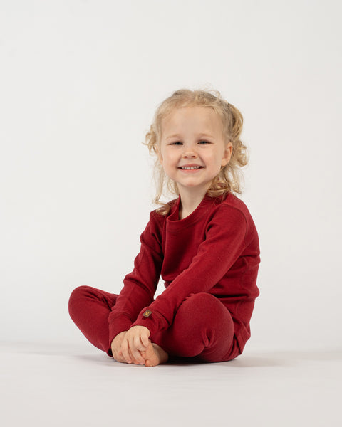 Child wearing a menique merino wool royal cherry outfit sitting on a white background