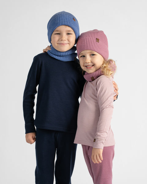 Two children modeling matching knit winter clothing sets against a light gray studio background. The boy wears a blue beanie and matching neck warmer with dark navy long-sleeve top and pants.