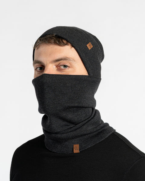 Person wearing a dark gray knit beanie and scarf set on a light gray background