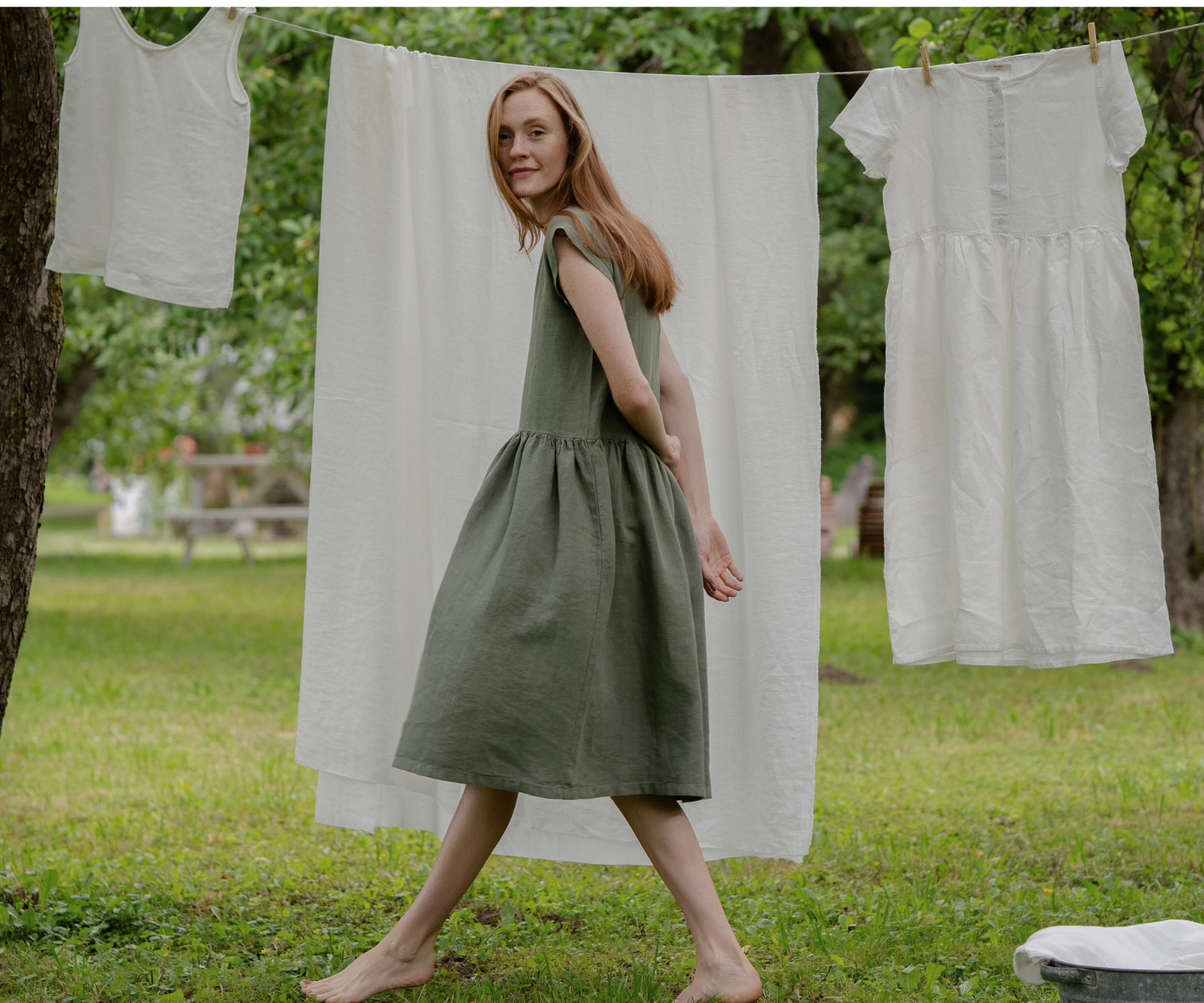 Woman in green linen dress near outdoor clothesline with natural fabrics