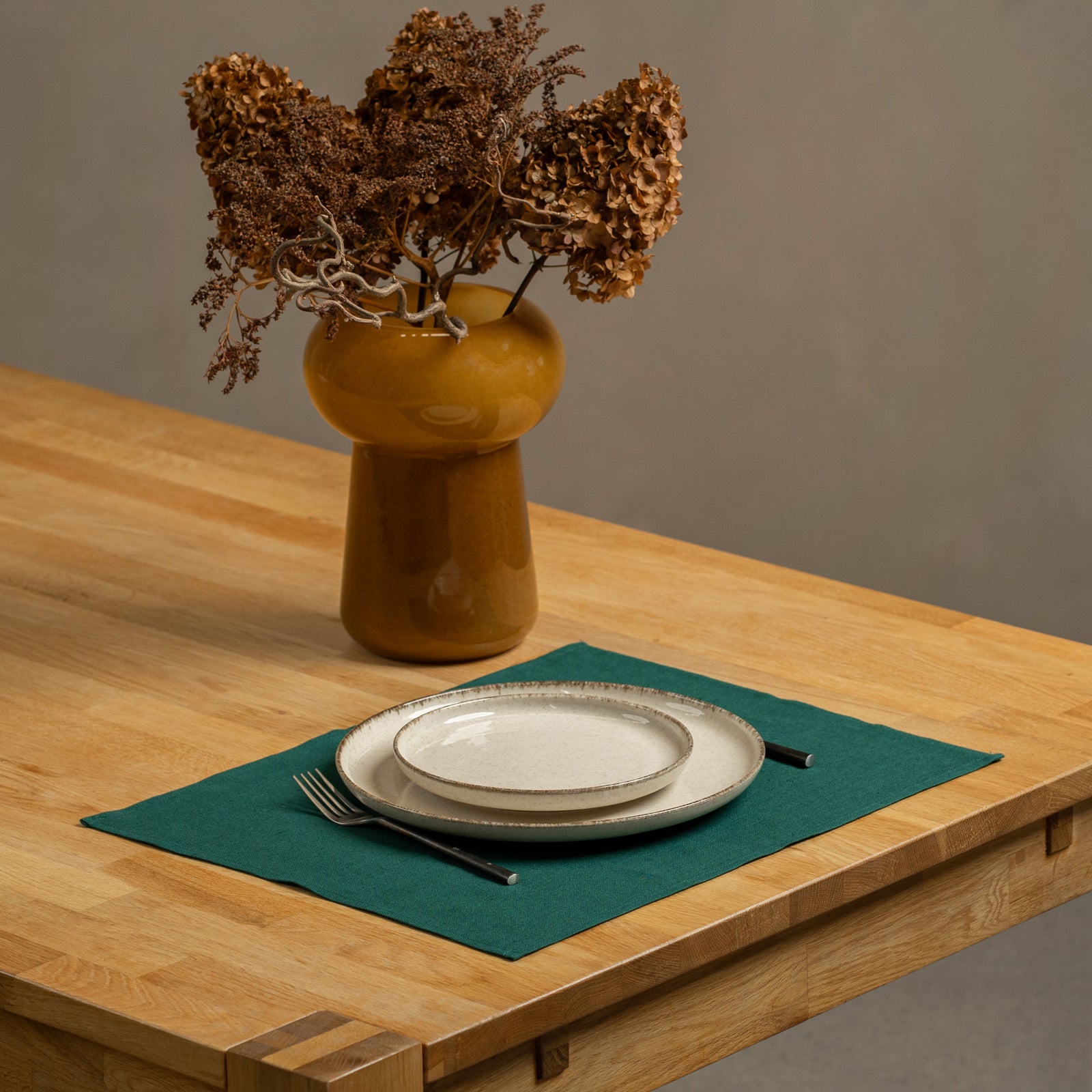 Spicy yellow linen placemat on a cozy fall dining table with pumpkins, pinecones, candles, and an autumn centerpiece.