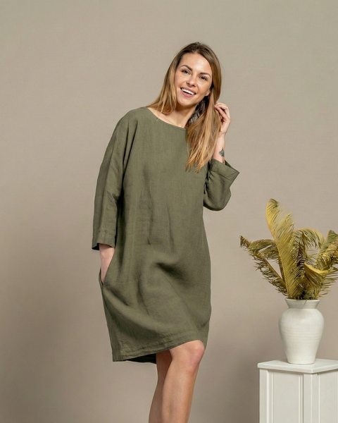 Woman in stone green linen dress with pockets, natural linen texture, neutral background.