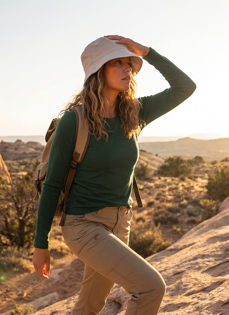 A woman wearing a light-colored hat and a green top looking out over a rocky, canyon-like landscape during golden hour.