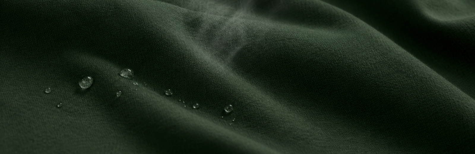 A macro shot of dark green, finely knit fabric with several clear water droplets resting on its surface, highlighting its texture and moisture-resistance.