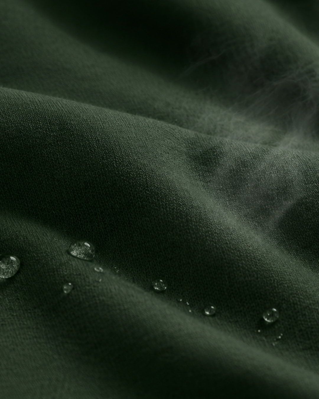 A macro shot of dark green, finely knit fabric with several clear water droplets resting on its surface, highlighting its texture and moisture-resistance.