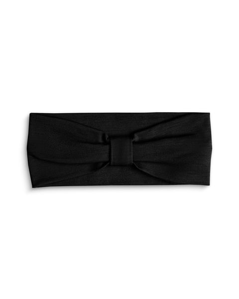 A product shot of a solid black fabric headband laid flat against a plain white background. The headband features a gathered center detail with a matching fabric wrap, creating a subtle bow or ribbon effect.