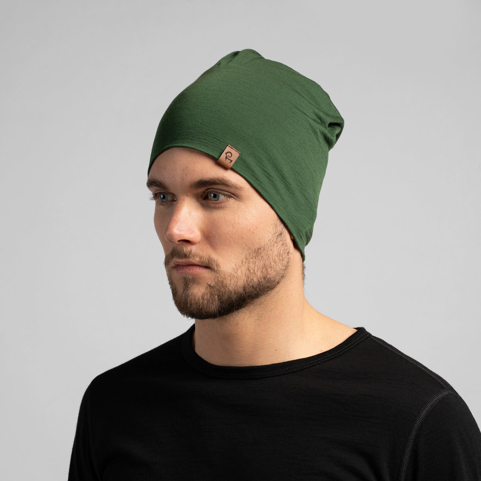 A half body upper body picture of a couple wearing unisex dark green menique merino headbands. They are smiling, the woman is leaning on the man's shoulder. They are also wearing black long sleeve merino tops.