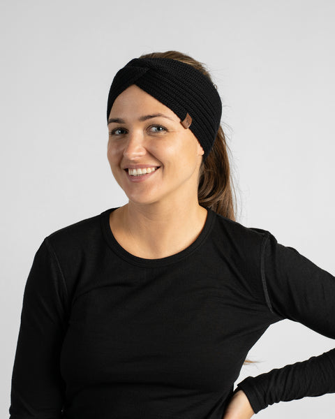 A woman wearing a black long-sleeve top and a black knit headband, posing with one hand on her hip while looking slightly to the side.