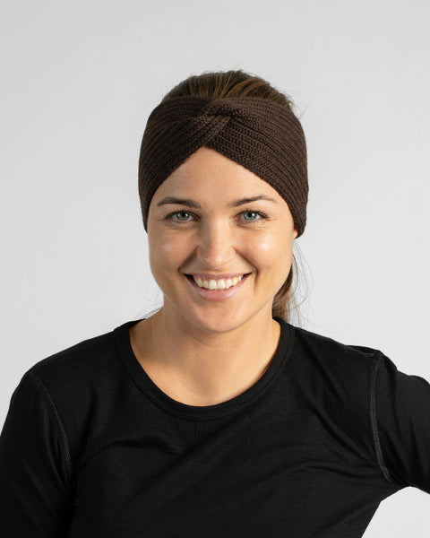 A chest-up studio portrait of a smiling woman wearing a black long-sleeve shirt and a dark brown knit headband.