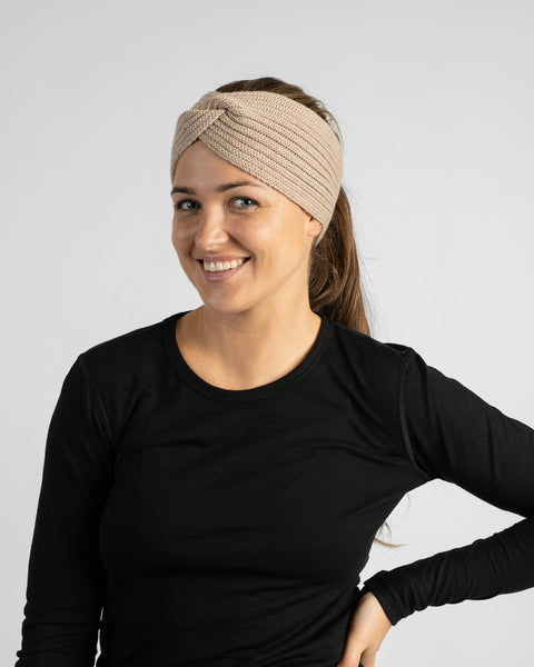 A woman wearing a black long-sleeve shirt and a light beige knit headband, posing with one hand on her hip while glancing aside.
