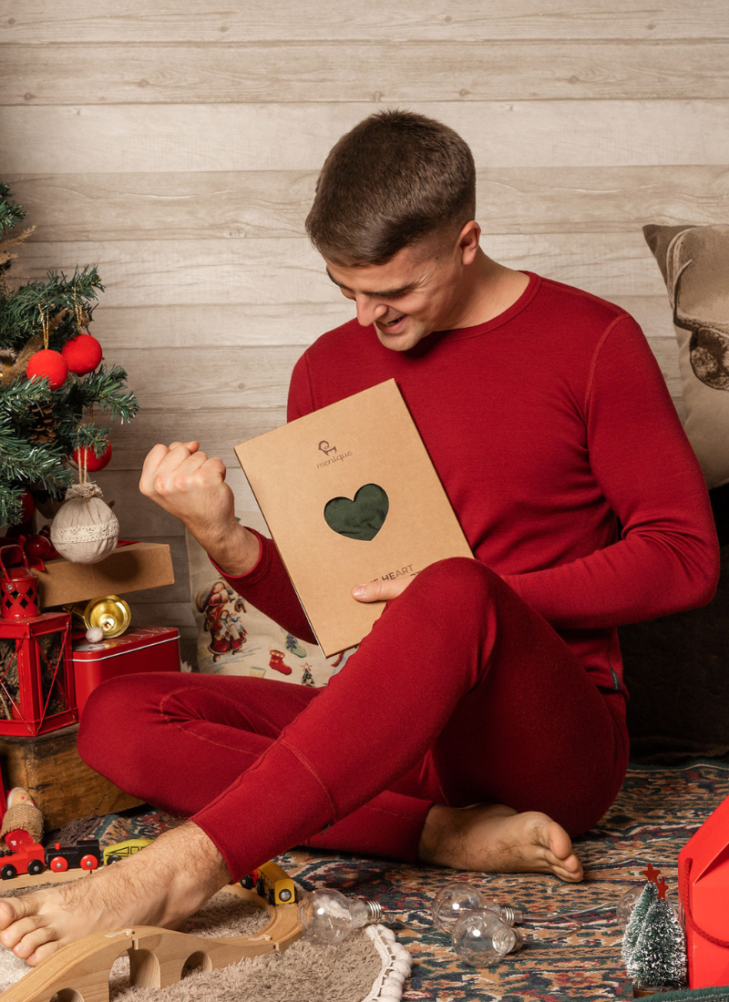 Man in red loungewear holding gift, sitting in cozy holiday setting