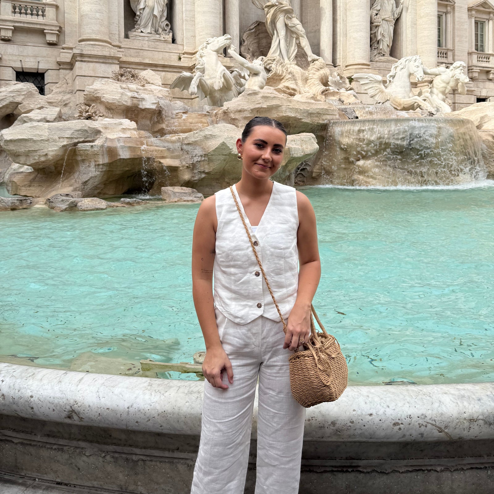 Woman in white outfit standing in front of a large fountain with classical architecture