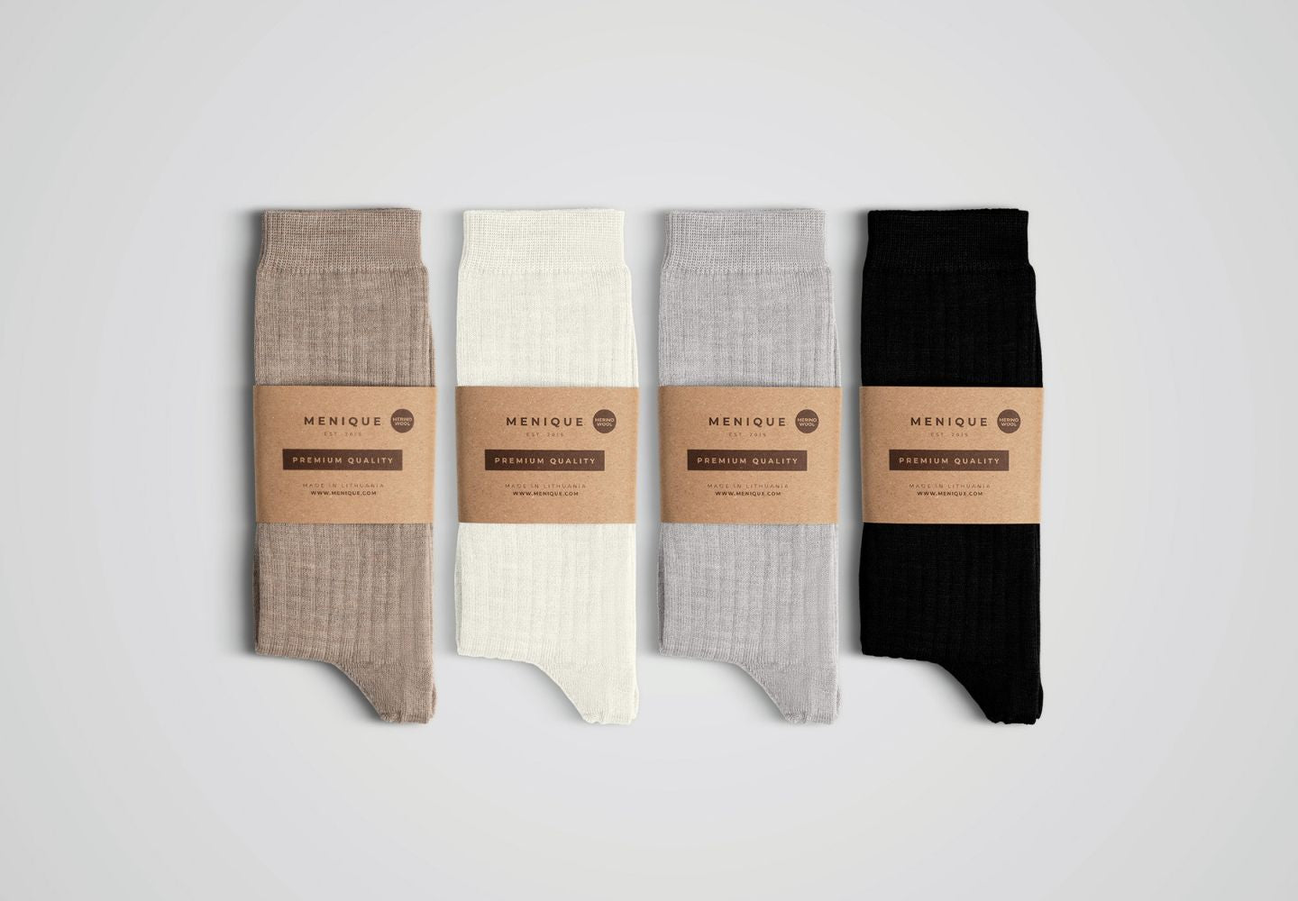 A flat-lay product shot of four pairs of ribbed socks lined up vertically against a plain light grey background. From left to right, the sock colors are light brown, off-white, light grey, and solid black. Each pair is bundled together with a brown kraft paper sleeve printed with the brand name "MENIQUE" and the words "PREMIUM QUALITY".