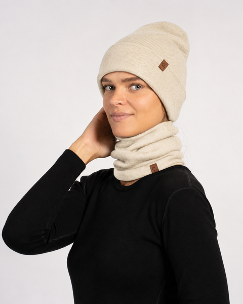 Smiling woman in a black long-sleeve shirt wearing a beige beanie and a matching beige neck gaiter around her neck.