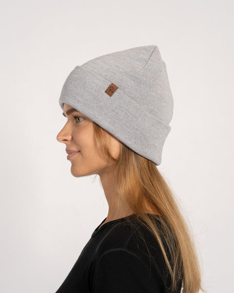 Woman in a light gray knitted merino wool beanie, looking left in profile while wearing a black top.