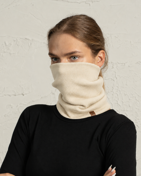 Woman in a black t-shirt wearing a beige neck gaiter pulled up over her nose and mouth.