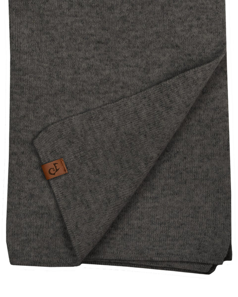 A close-up flat lay of a dark charcoal grey knitted scarf. A corner of the hem is folded up diagonally, displaying a small, rectangular brown leather logo patch. The texture of the fine knit is visible against the pure white background.