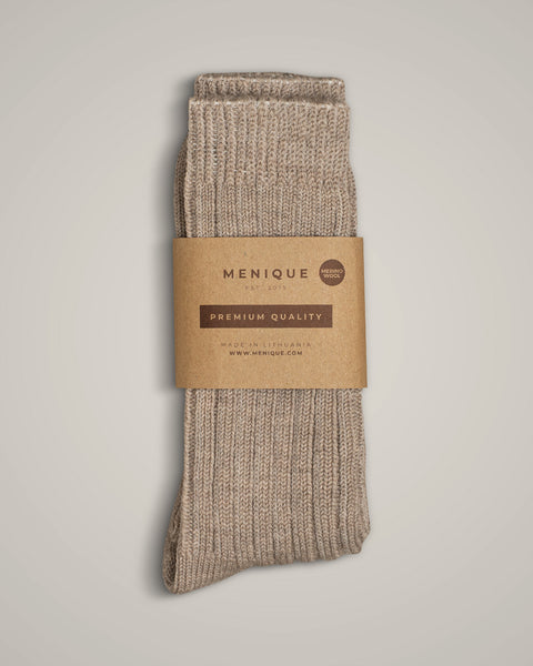 Beige ribbed merino wool socks by Menique, folded neatly with a brown eco-friendly paper label reading “Premium Quality – Made in Lithuania.” The socks have a thick, cozy knit texture, displayed on a light neutral background.