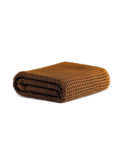 A neatly folded, dark rust-orange waffle-weave towel isolated on a pure white background. The deep waffle texture is clearly visible.