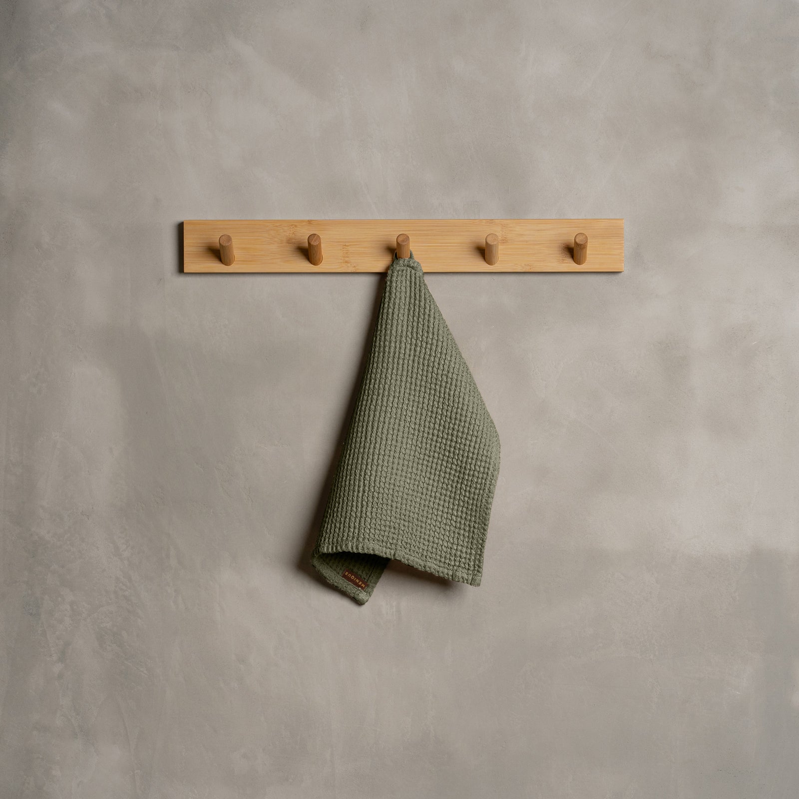A woman holding a waffle washcloth Face Towel of 30x30cm dimensions by her face, in Sand Brown color.