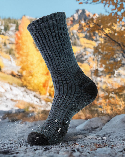 Dark gray hiking sock on a rocky surface with autumn foliage in the background